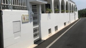 Un edificio blanco con entrada protegida por un portón, varias ventanas de arco y plantas en macetas.