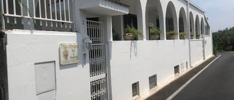 A white building with a gated entrance, multiple arched windows, and potted plants.