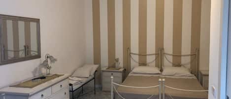 Un dormitorio con cama, mesitas de noche, cómoda, espejo y pared a rayas.