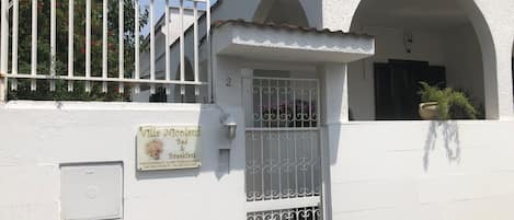 A white building with a sign for Villa Nicolas Bed & Breakfast, featuring a metal gate and a potted plant.