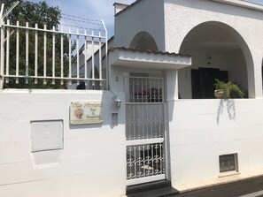 A white building with a sign for Villa Nicolas Bed & Breakfast, featuring a metal gate and a potted plant. - Villa Nicolaus (Bari)