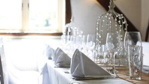Una mesa de comedor dispuesta con servilletas blancas, copas de vino transparentes y una jaula decorativa de cristal.