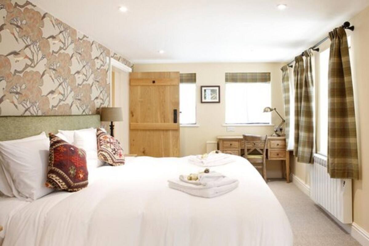 Une chambre d’hôtel avec un grand lit, une armoire en bois, un bureau et une fenêtre avec des rideaux.