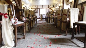 Un pasillo de iglesia con bancos de madera, pétalos de flores rojas en el suelo y cortinas blancas adornadas con lazos rojos.