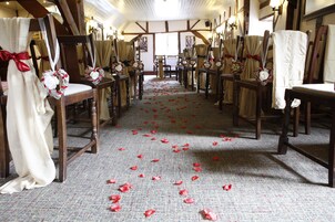 A church aisle with wooden pews, red flower petals on the floor, and white curtains with red bows.
