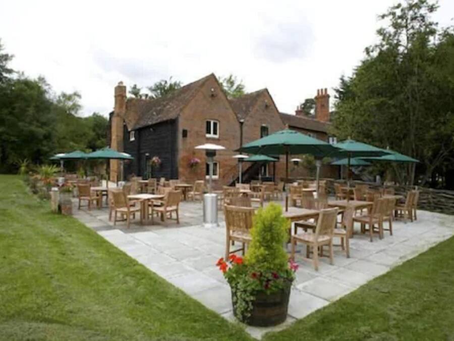 An outdoor patio area with multiple tables and chairs, surrounded by a brick building.