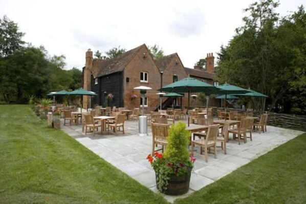 An outdoor patio area with multiple tables and chairs, surrounded by a brick building. - Barton's Mill (Basingstoke)