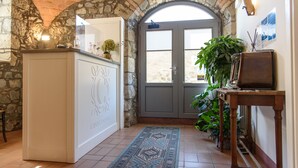 A hallway with a stone archway, a white cabinet with decorative carvings, a blue patterned rug, and a wooden table with a framed picture. - Casale 1541 (Bolsena)