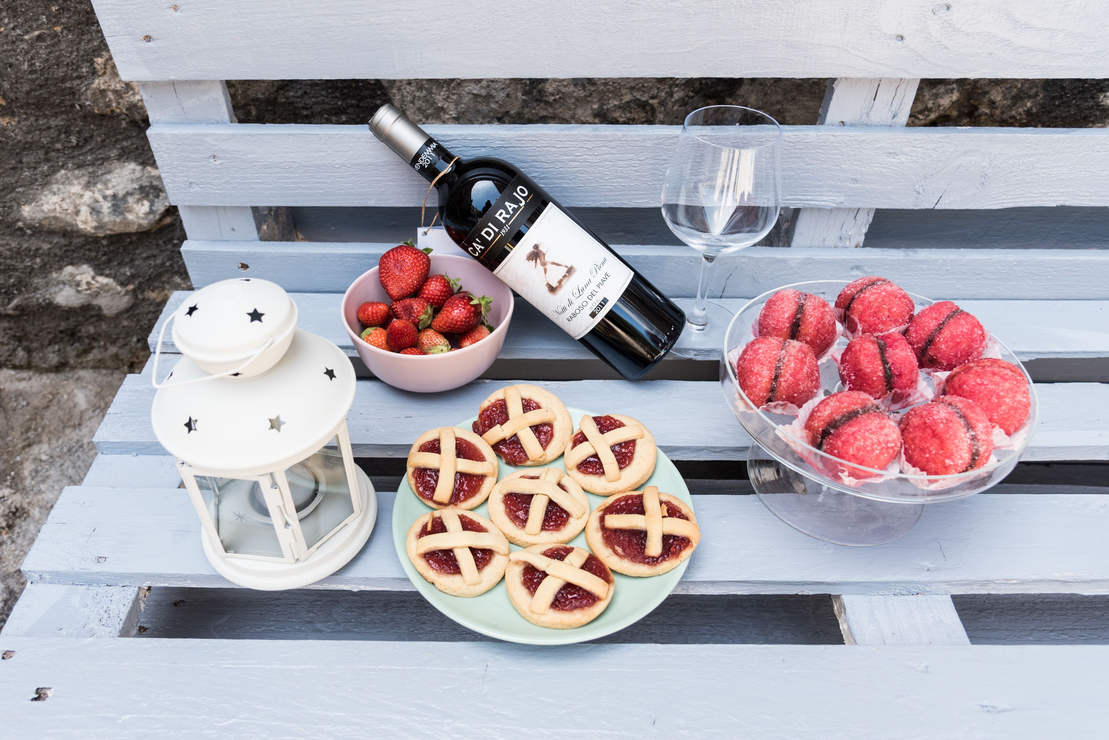 Une table avec une bouteille de vin, un verre, un bol de fraises et une assiette de biscuits.