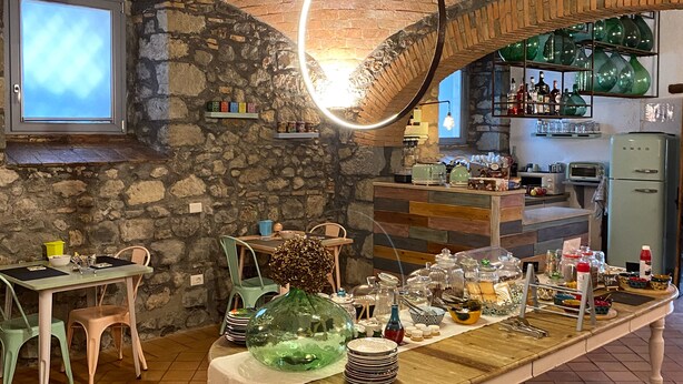 A rustic kitchen with a stone wall, a wooden dining table, and a hanging light fixture. - Casale 1541 (Bolsena)