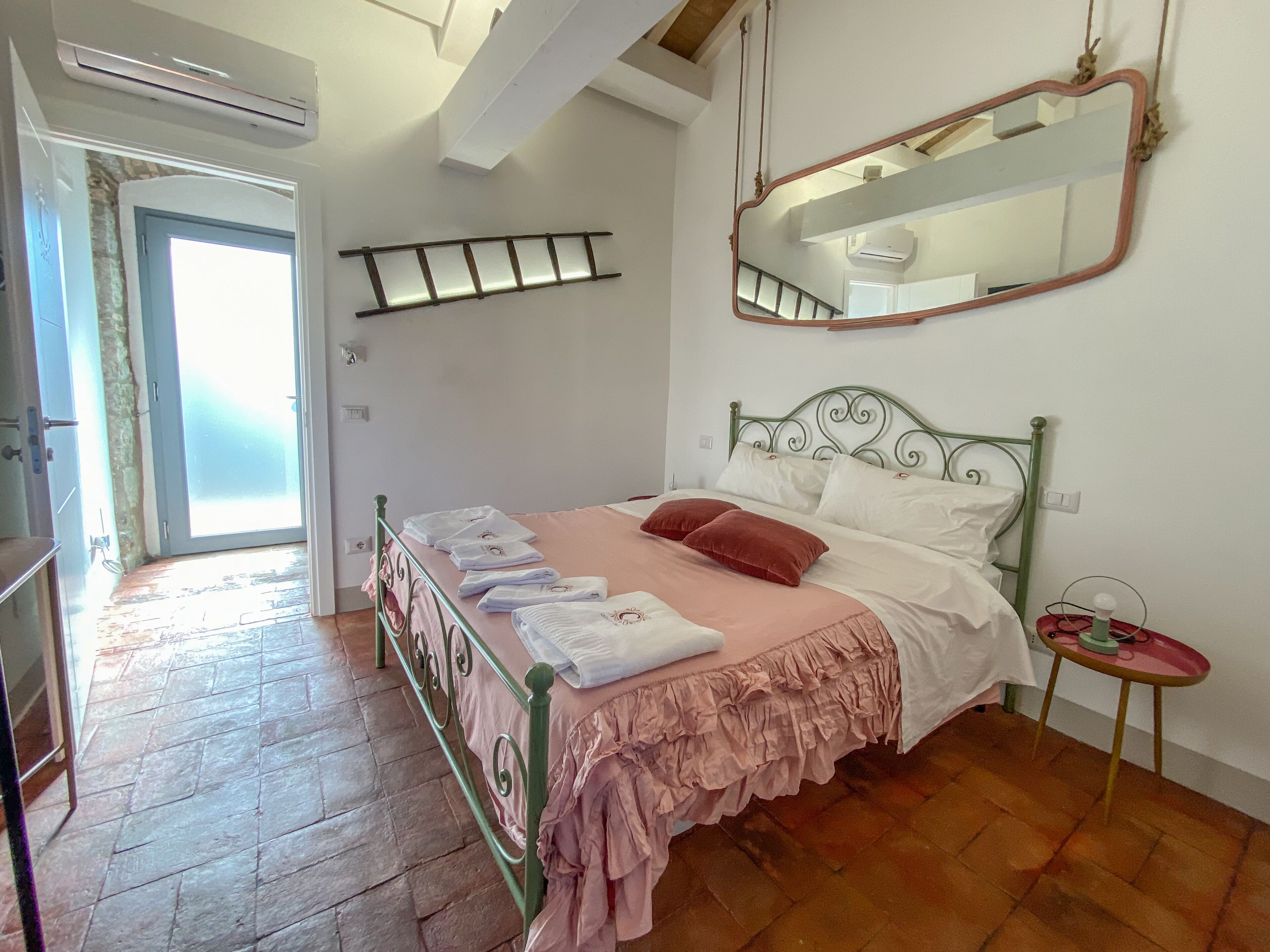 Un dormitorio con cama, mesita de noche, espejo y ventana.
