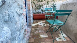 A stone-walled courtyard with a tiled floor, a green folding table, and a bench. - Casale 1541 (Bolsena)