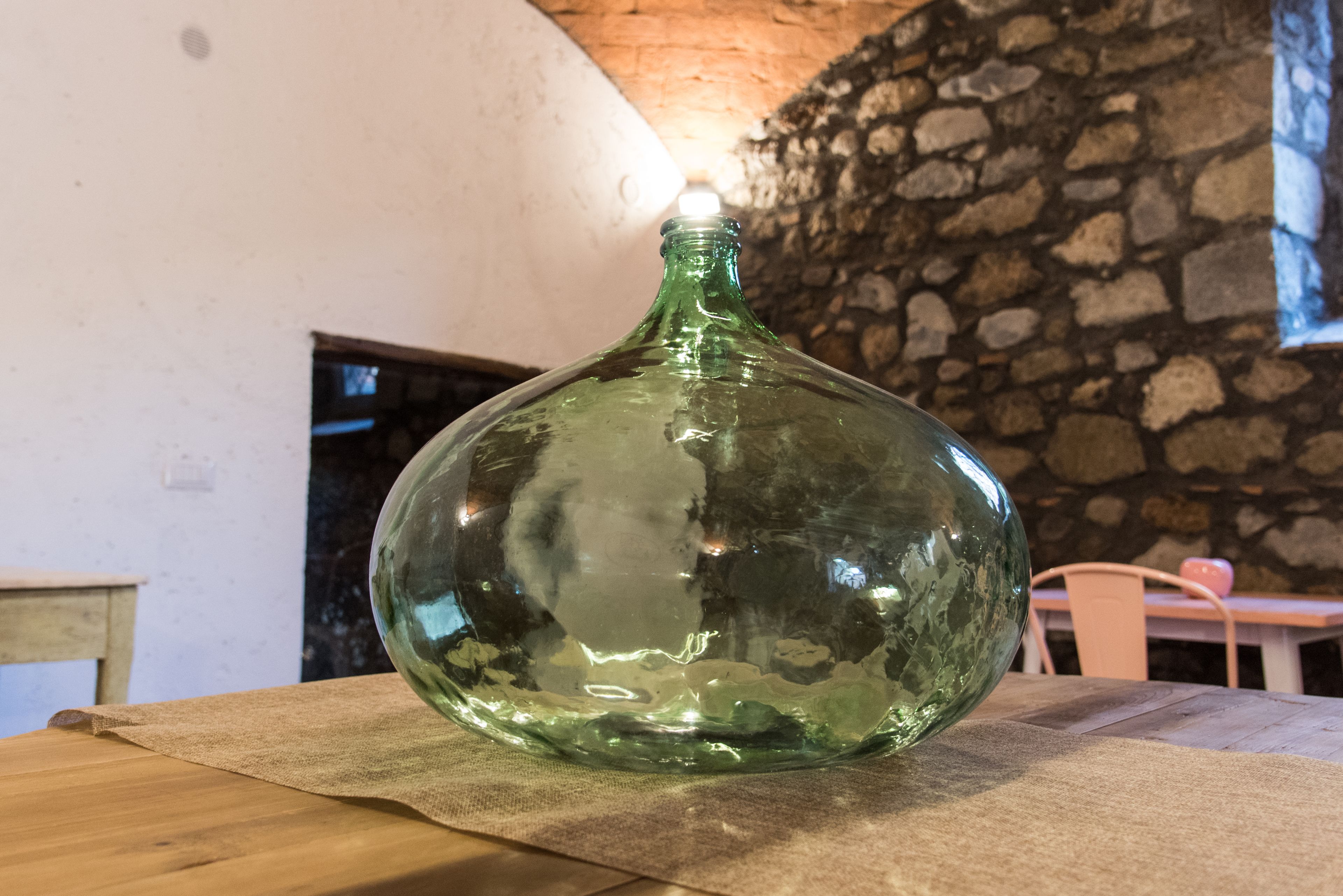 Una botella de vidrio verde sobre una mesa de madera en una habitación con paredes de piedra y techo blanco.