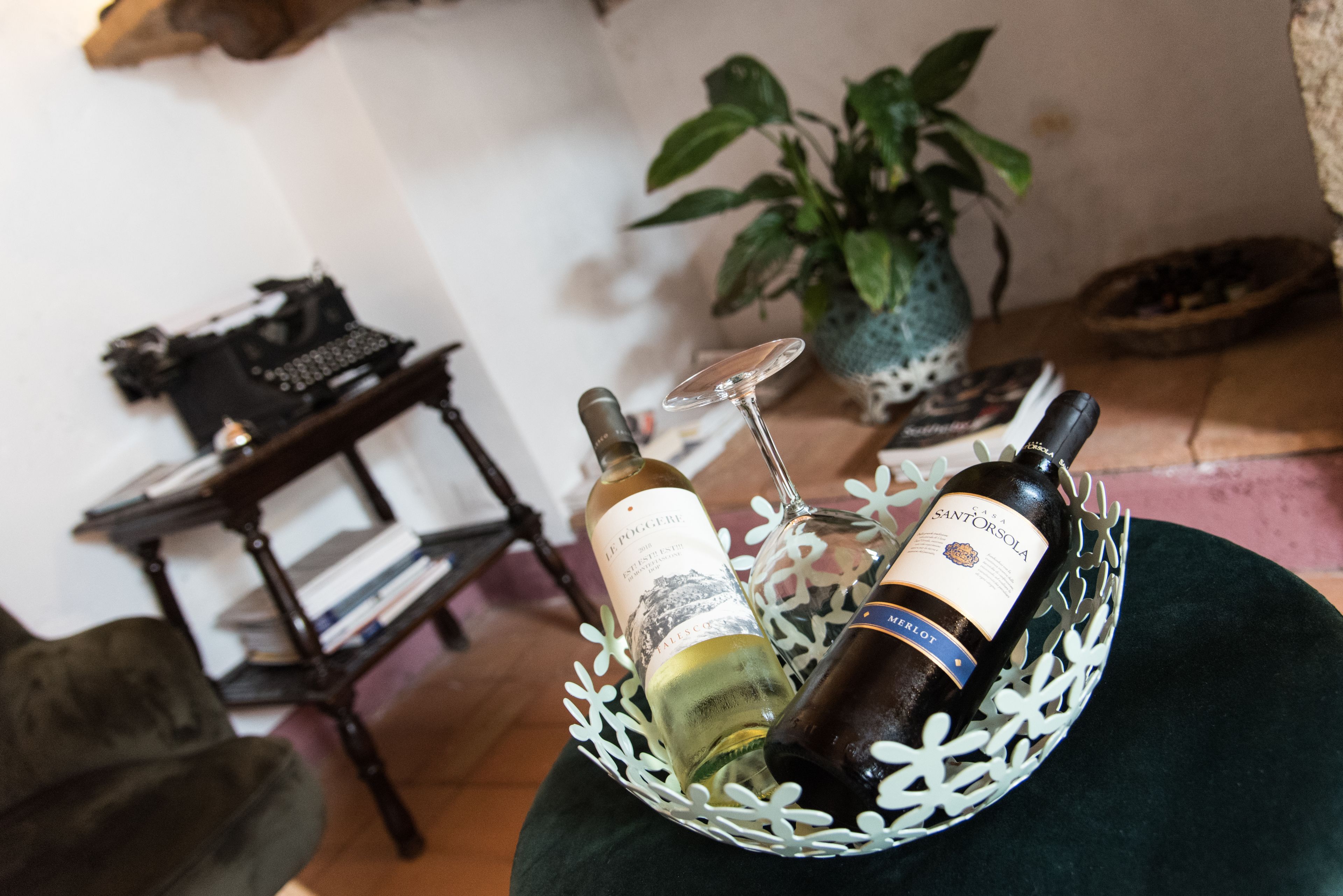A room with a wooden table, a potted plant, and a decorative metal basket containing two wine bottles.