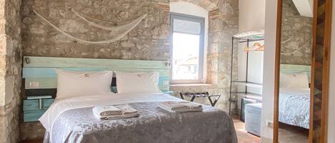 Une chambre avec un mur en pierre, un lit doté d’une tête de lit bleue, une fenêtre et un miroir.