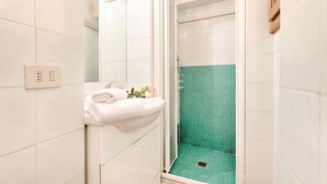 Un baño con un lavamanos blanco, una ducha con azulejos verdes y una toalla blanca sobre el lavamanos.
