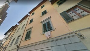 Un edificio de varios pisos con fachada color beige, contraventanas verdes y ropa tendida a la vista.