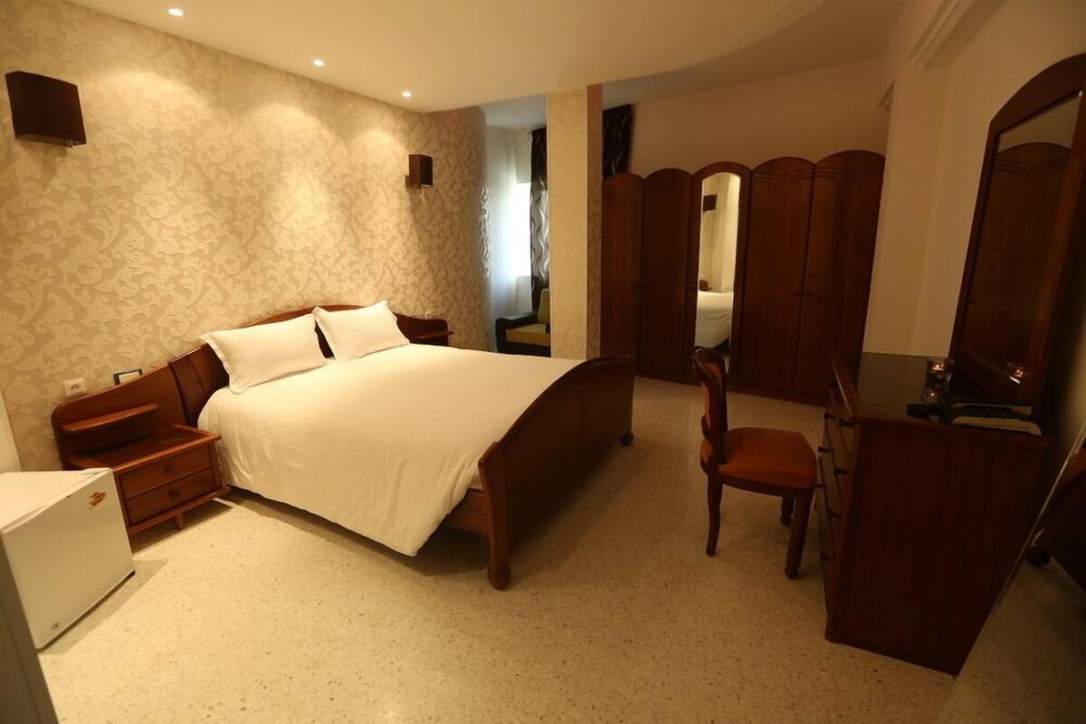 Un dormitorio con una cama grande, mesitas de noche de madera, un aparador y un espejo.