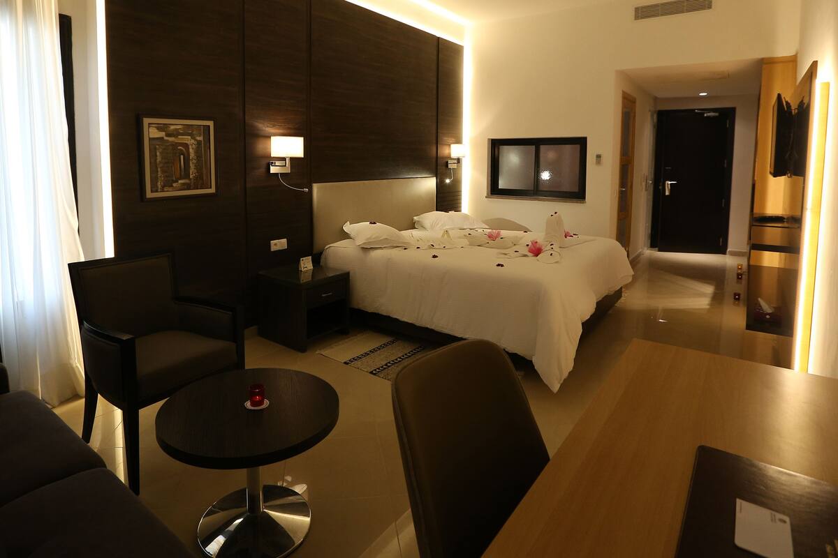 Habitación de hotel con cama, mesita de noche, una silla, una mesita redonda y una lámpara de pared.
