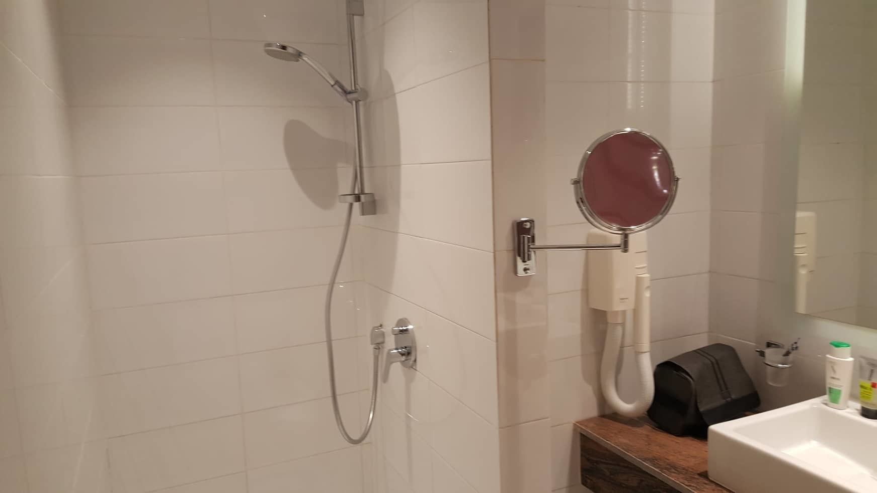 A bathroom with a shower, a mirror, a sink, and toiletries.