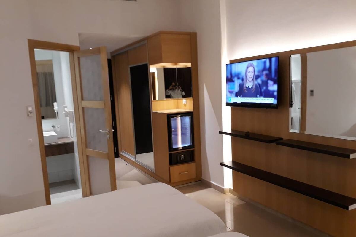 Una habitación de hotel moderna con cama, televisor montado en la pared, armario y espejo.