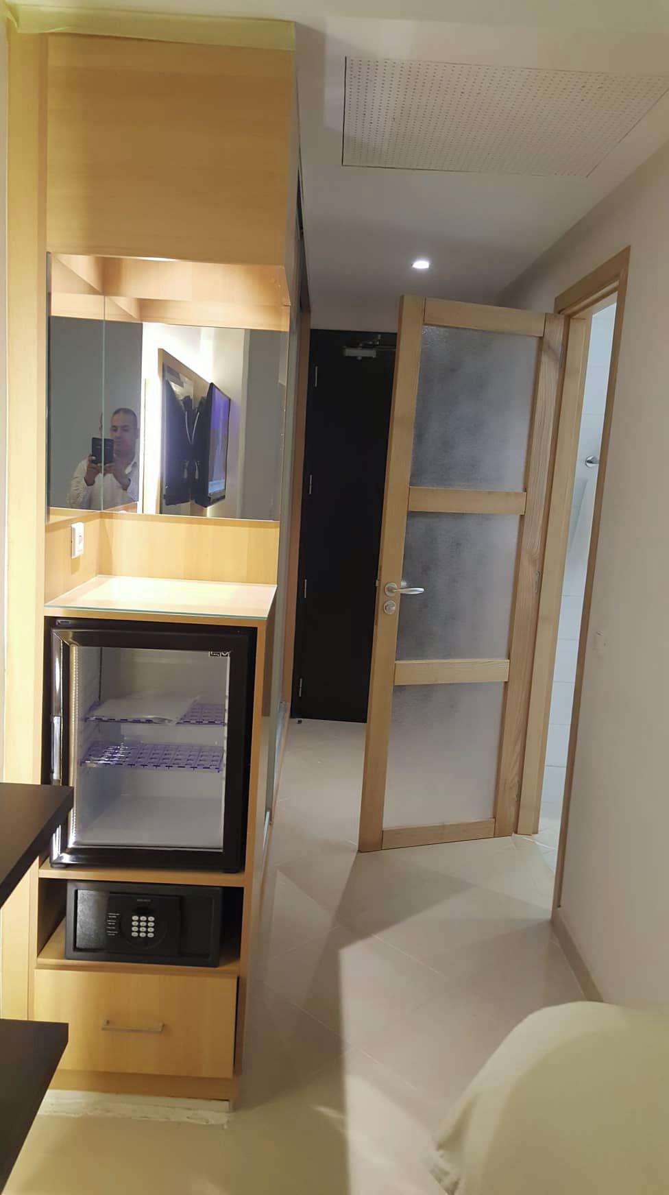 Una habitación pequeña con cama, microondas integrado, un mueble bajo y un espejo.