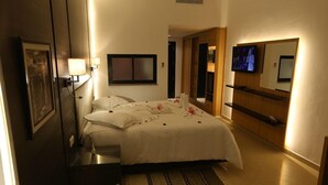 Hotellihuone, jossa on sänky, yöpöydät, televisio, peili ja puinen kaappi.