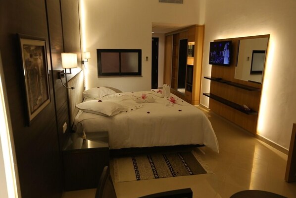 A hotel room with a bed, bedside tables, a TV, a mirror, and a wooden cabinet.