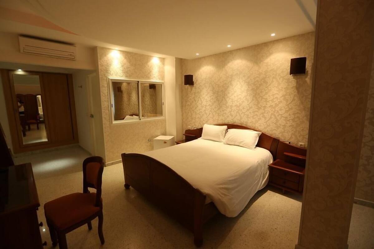 Un dormitorio con una cama grande, una silla, una mesita de noche y un espejo en la pared.