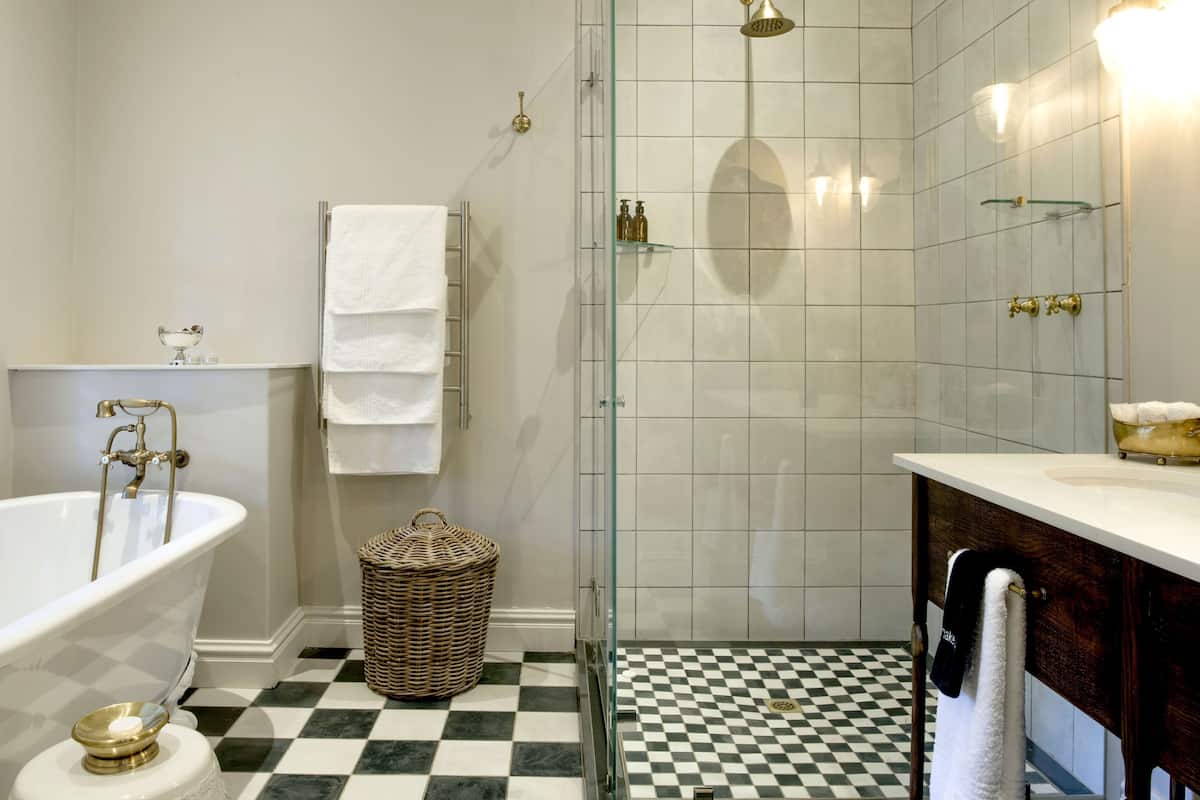Een badkamer met een vrijstaand bad, een glazen douchecabine, een zwart-wit geruite vloer en een houten wastafelmeubel.