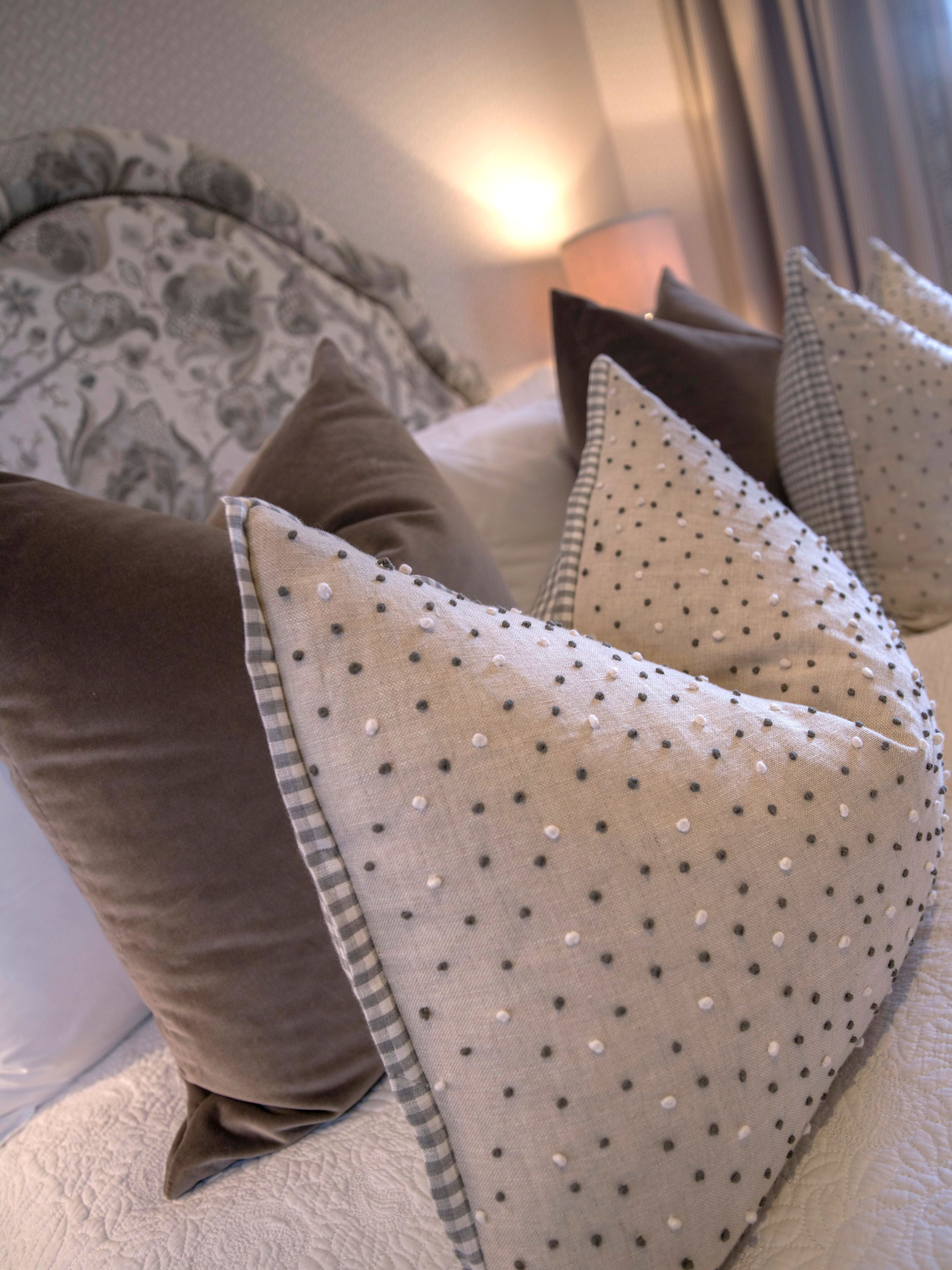 A bed with a patterned headboard, a pillow with a polka dot design, and a checkered pillow.