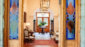 A grand hallway with a wooden floor, a central table with a vase of flowers, and two chairs. - Hartford House (Mooirivier)