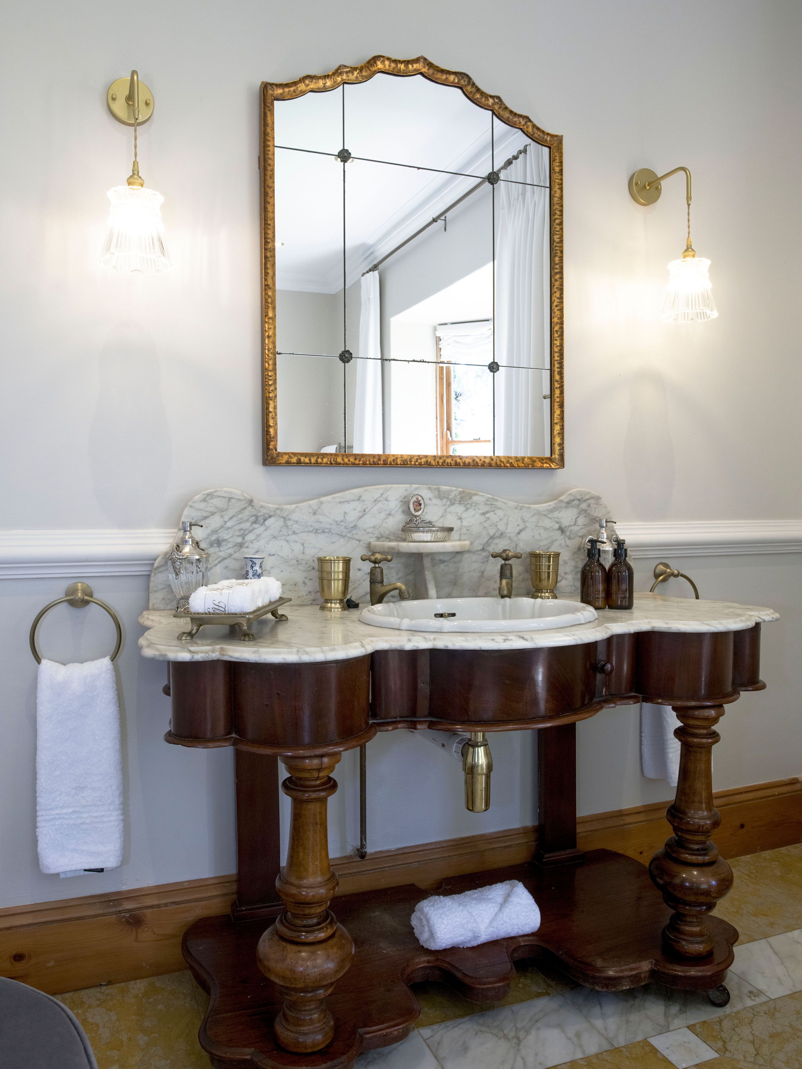 A bathroom with a marble sink, gold fixtures, and a large mirror.