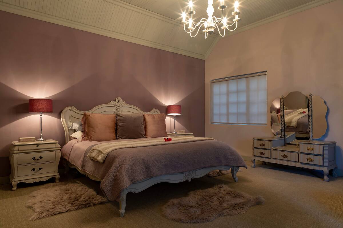 Een slaapkamer met een groot bed, twee nachtkastjes, een dressoir, een spiegel en een kroonluchter.