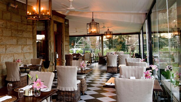 A restaurant with a checkered floor, wicker furniture, and hanging lanterns. - Hartford House (Mooirivier)