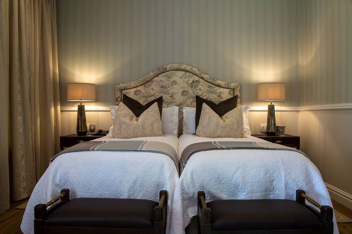 Een tweepersoonsbed met een bloemenprint hoofdbord, twee nachtkastjes met lampen, en een gordijn aan de linkerkant.