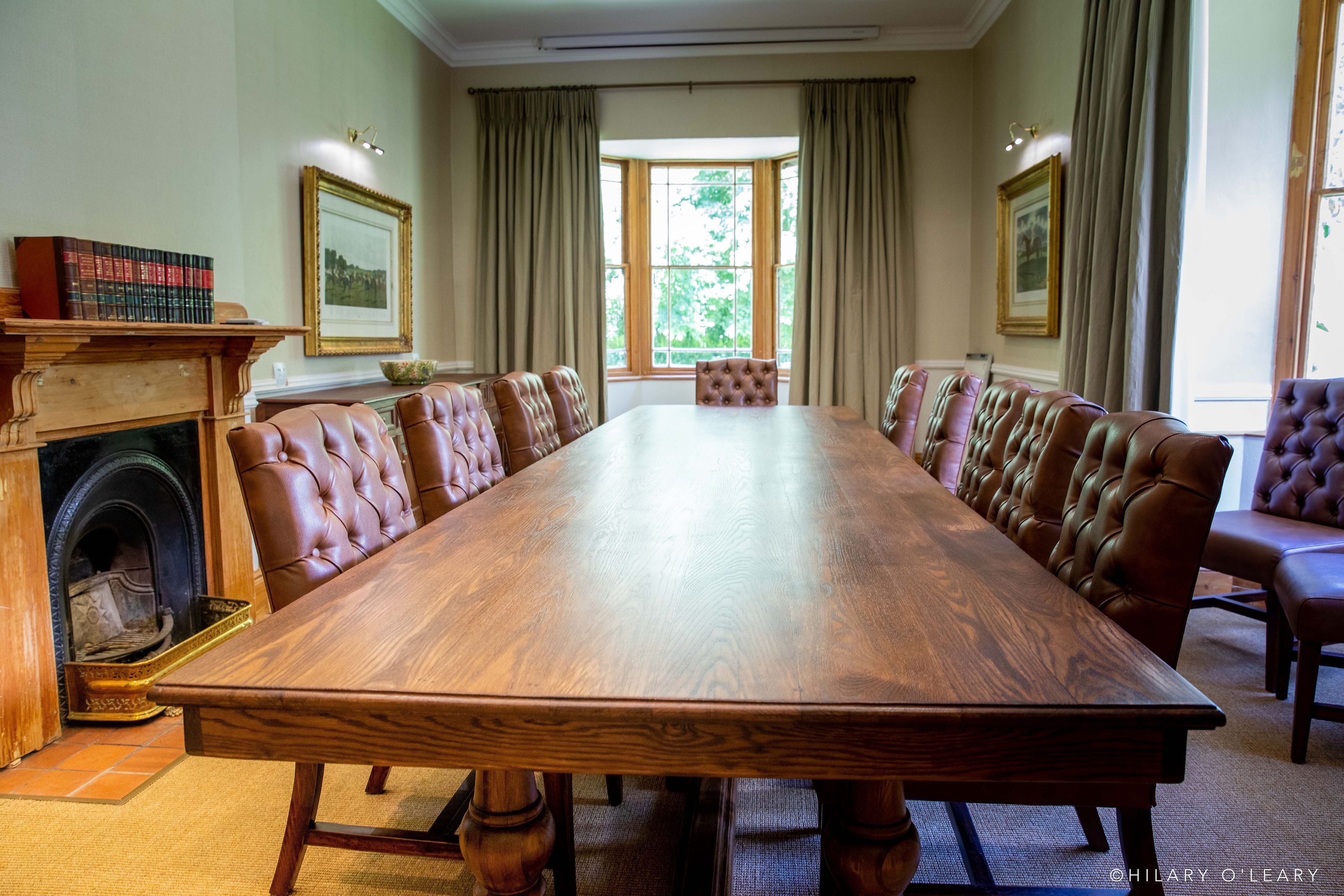 Een vergaderruimte met een lange houten tafel, lederen stoelen, een open haard en kunstwerken in lijsten aan de muren.