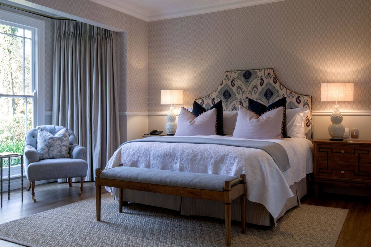 Een slaapkamer met een groot bed, twee bedlampen, een houten bankje, een stoel en een nachtkastje.
