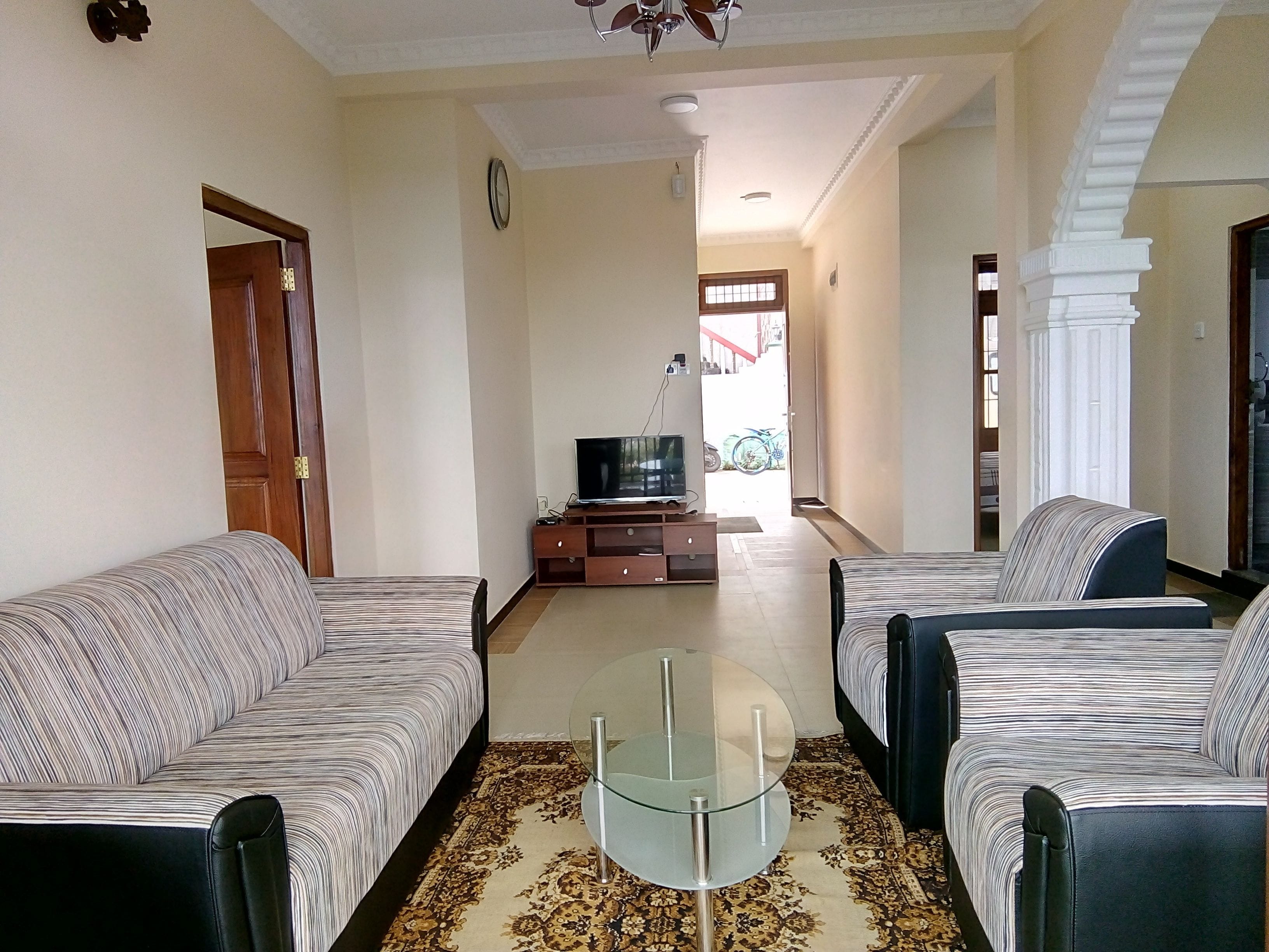 A living room with two sofas, a glass coffee table, a TV on a wooden stand, and a patterned rug.