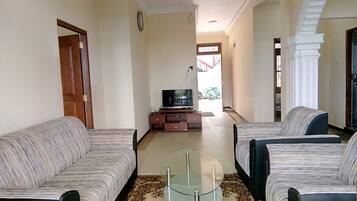 A living room with two sofas, a glass coffee table, a TV on a wooden stand, and a patterned rug.