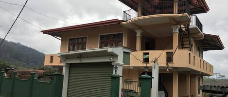 A two-story building with a green gate, a closed garage door, and a parked scooter.
