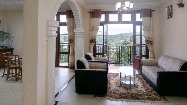 Un salon comprenant un canapé, des fauteuils, une table basse et un balcon offrant une vue sur la campagne.