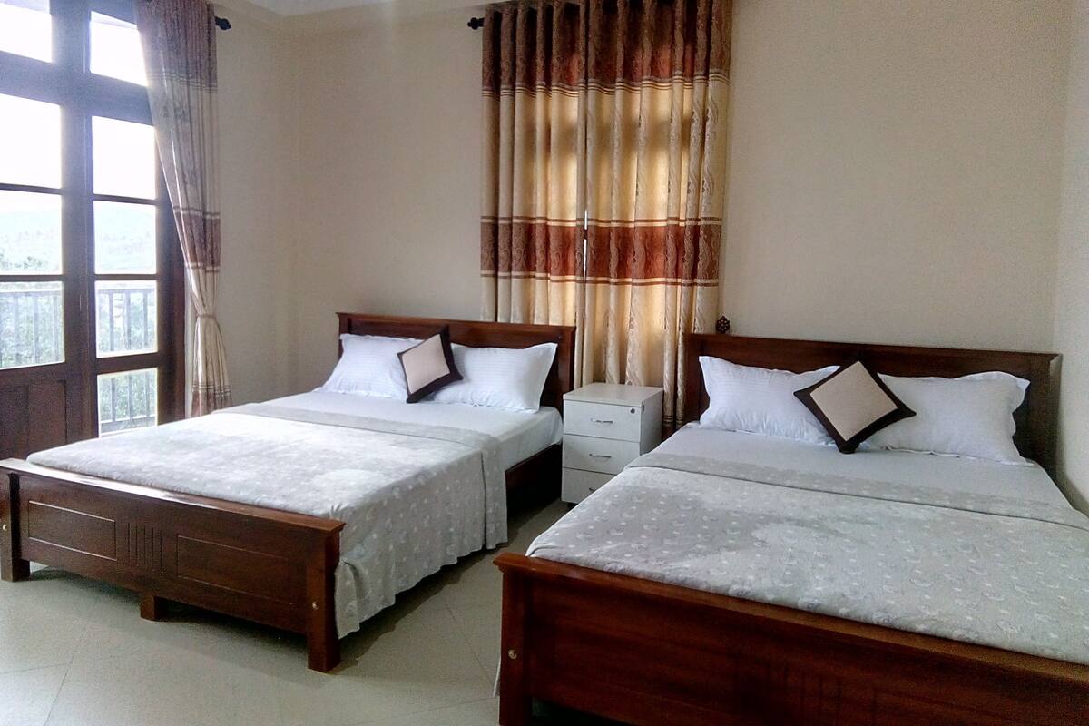 A hotel room with two wooden beds, a nightstand, and a window with curtains.