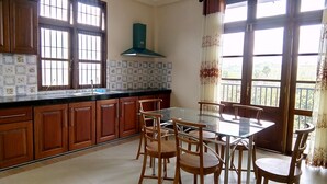 Une cuisine avec des meubles en bois, un pare-feu en carrelage, une grande fenêtre avec des rideaux et une table à manger avec des chaises.