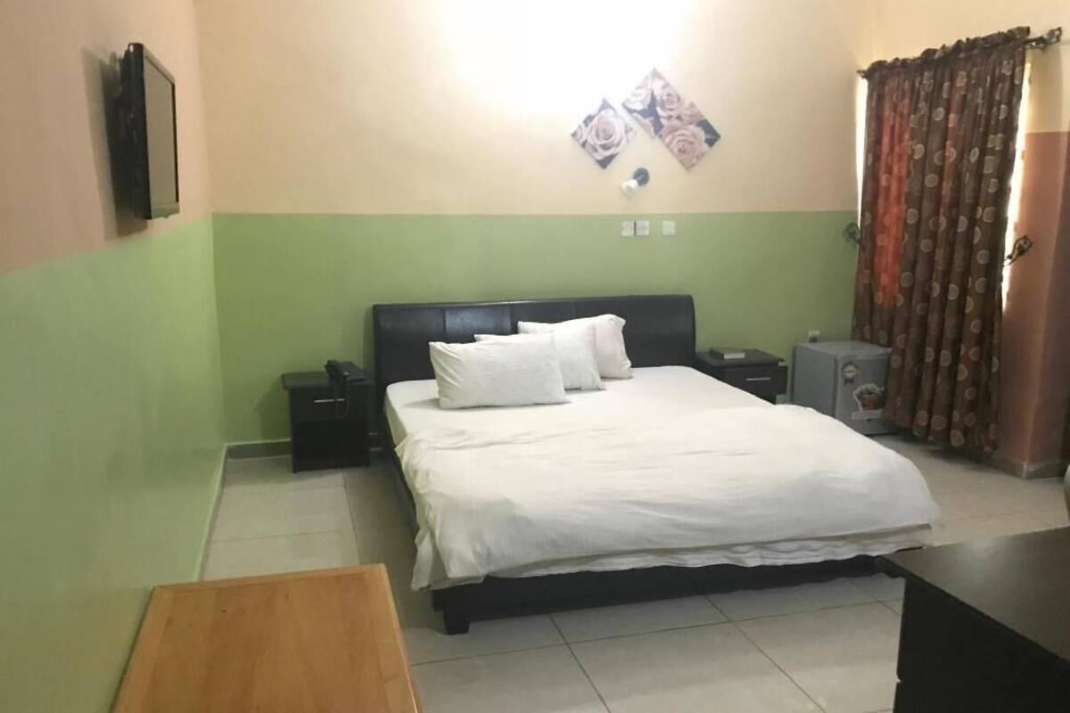 A bedroom with a bed, bedside tables, a desk, a chair, and a wall-mounted TV.