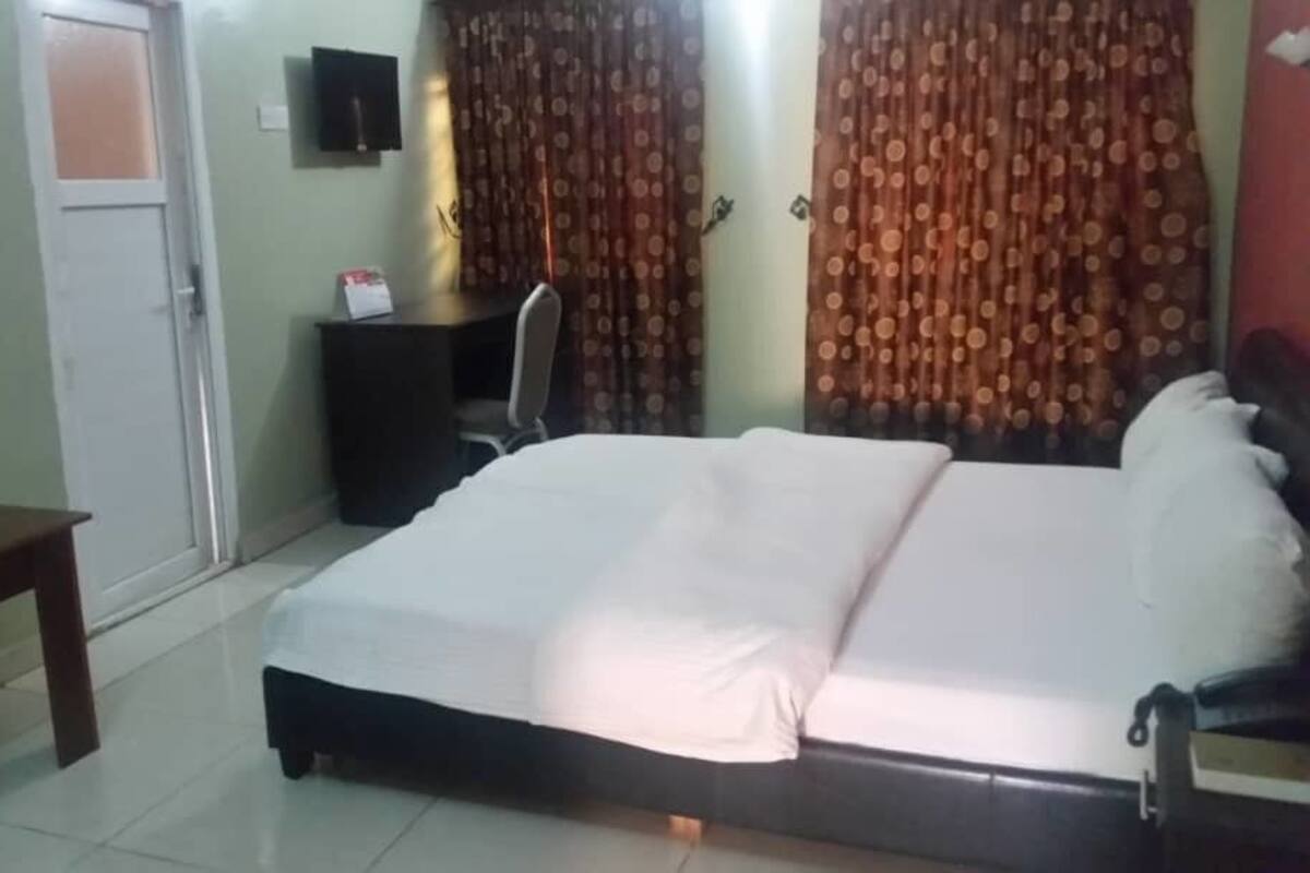 A hotel room with a bed, a desk, a chair, and curtains.