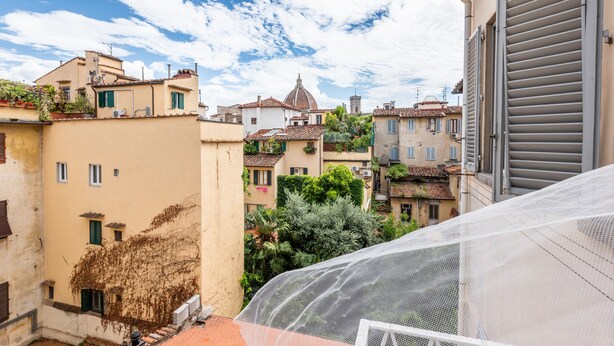 Une rue étroite bordée de bâtiments des deux côtés, un ciel dégagé et, au loin, on aperçoit le dôme d’une église.