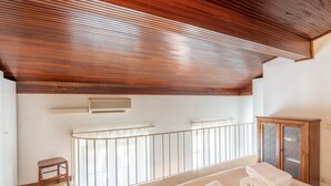 Une pièce avec un plafond en bois, un lit avec des serviettes pliées, un petit tabouret et un meuble avec des portes en verre.