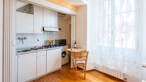 Une cuisine compacte avec des meubles blancs, un lave-linge, un four à micro-ondes et un coin repas équipé d’une chaise.