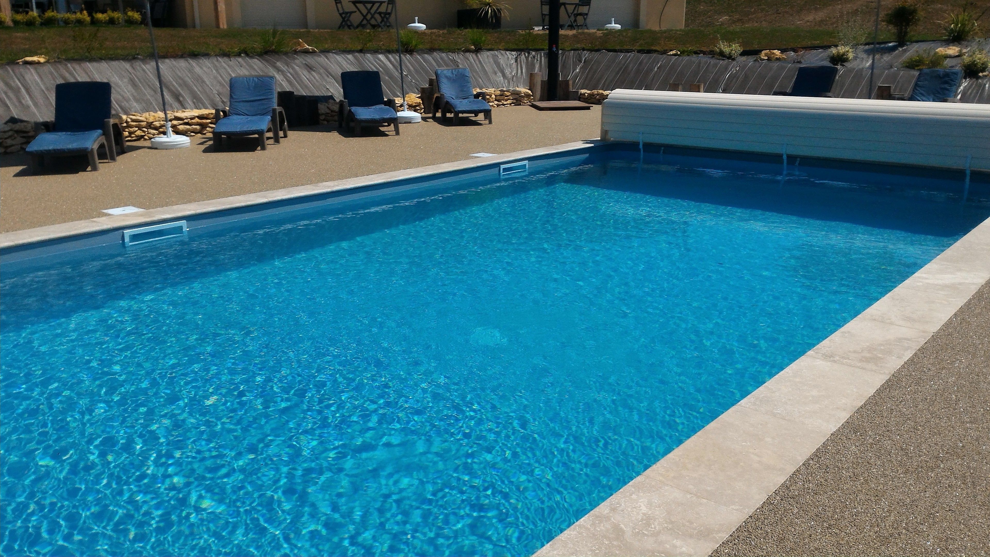 A clear blue swimming pool with lounge chairs and a stone wall in the background.